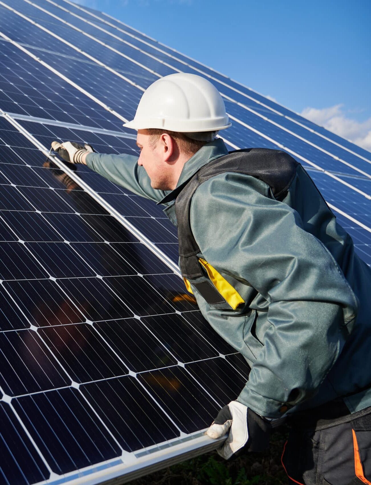 Man technician in Solar Power Specialist waring a safety helmet repairing photovoltaic solar module. Electrician in gloves maintaining solar photovoltaic panel system. Concept of alternative energy and power sustainable resources.