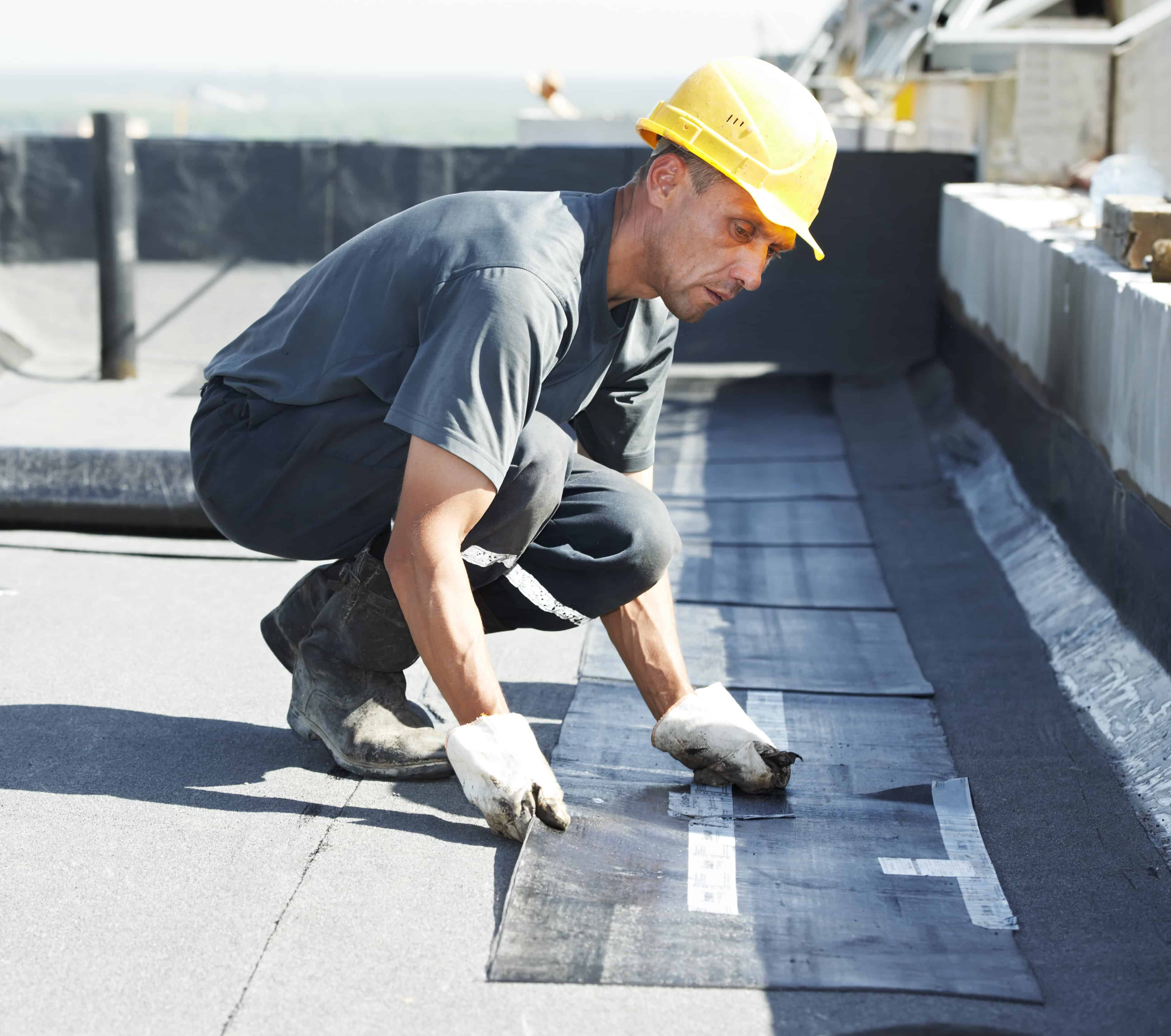 Flat Roofer preparing part of bitumen roofing felt roll for melting by gas heater torch flame