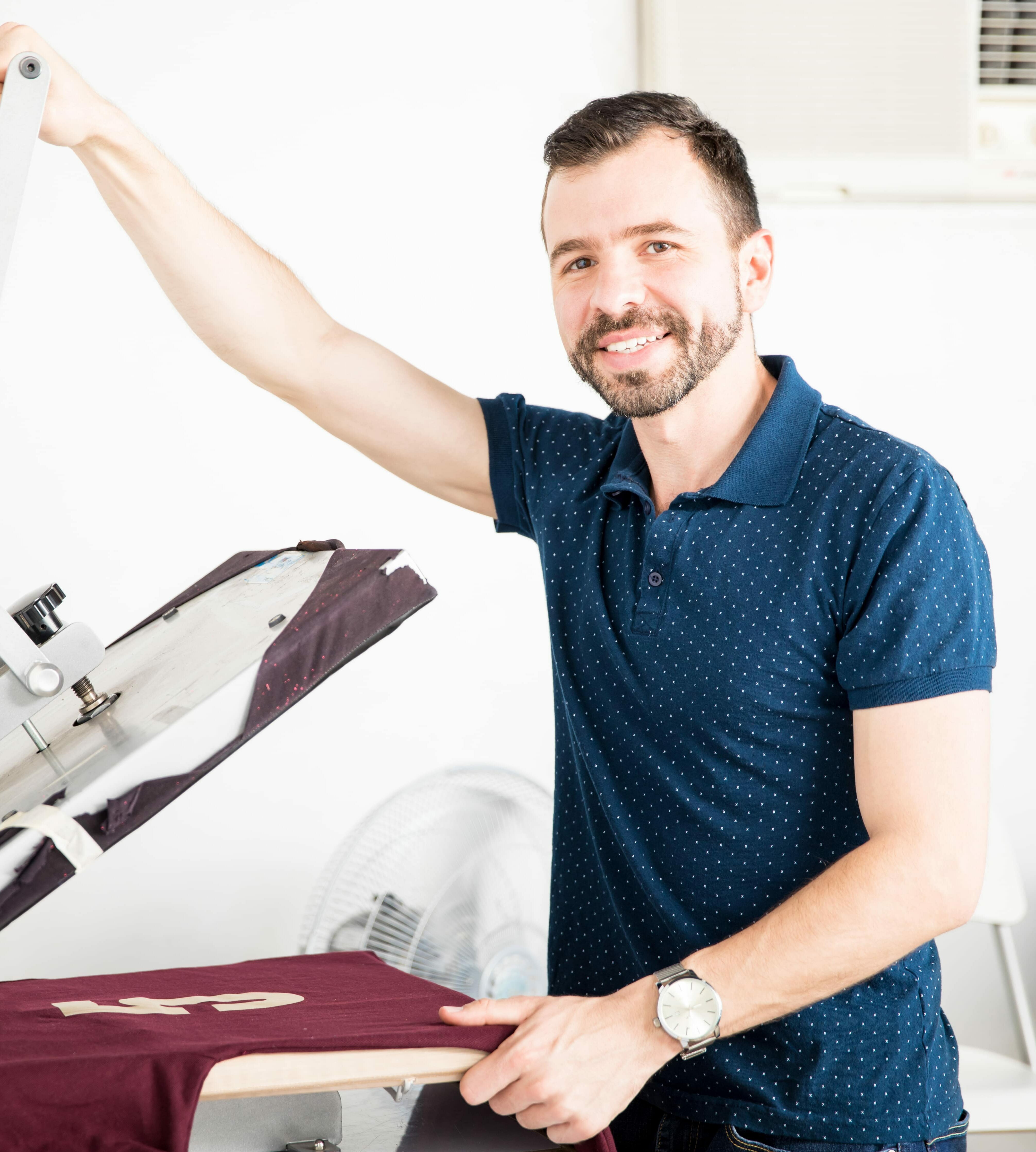 Portrait of a good looking Hispanic worker using a serigraph press for printing a shirt