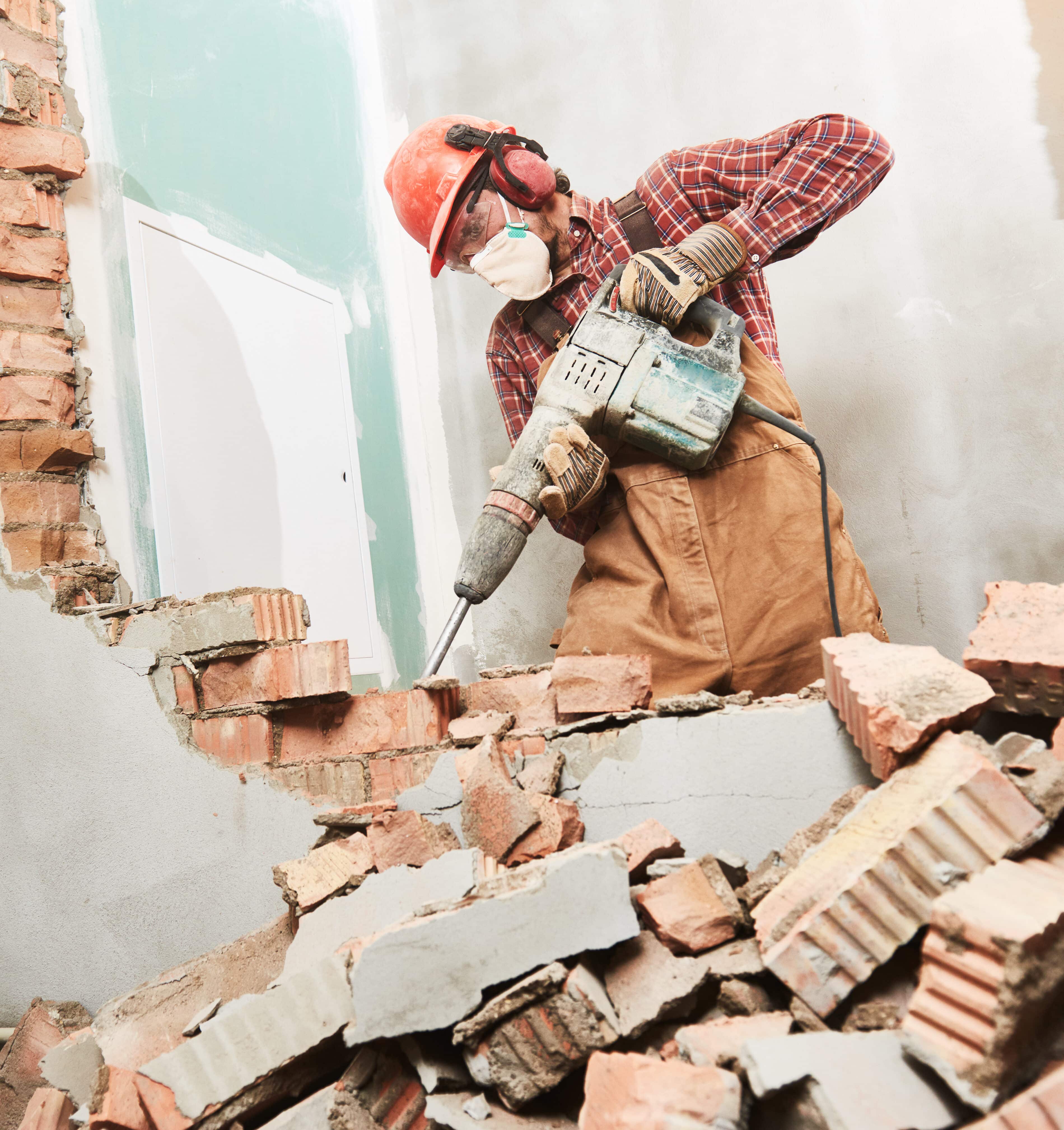 Worker with personal protection equipment and demolition hammer at service for interior brick wall construction breaking in building industry