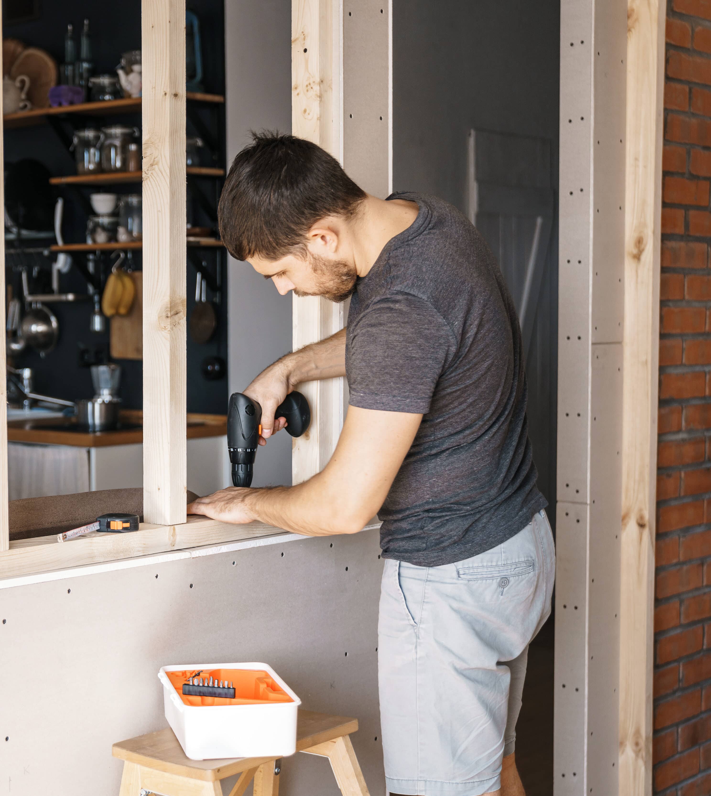 A man with a screwdriver in his hand fixes a wooden frame for a window in his house