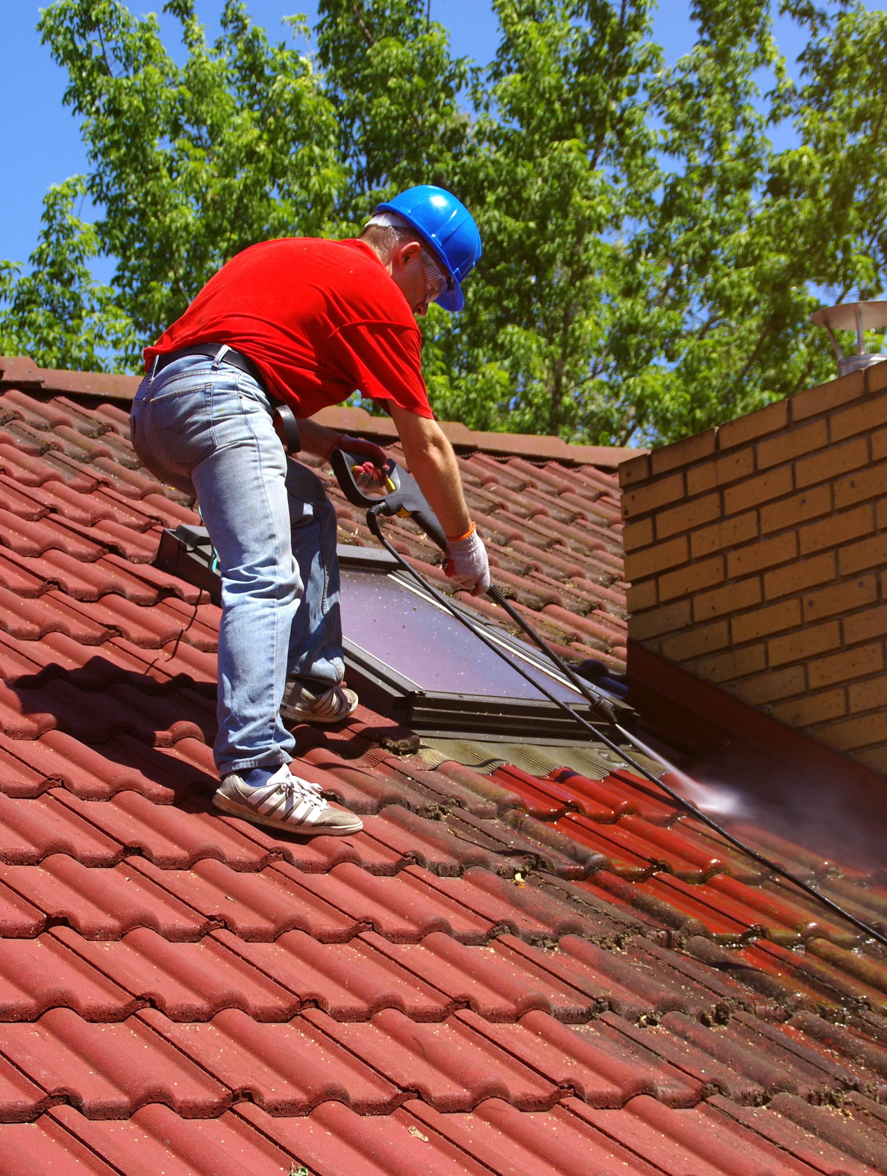 House roof cleaning with pressure tool. Worker on top of building washing tile with professional equipment. Moss removing with water.