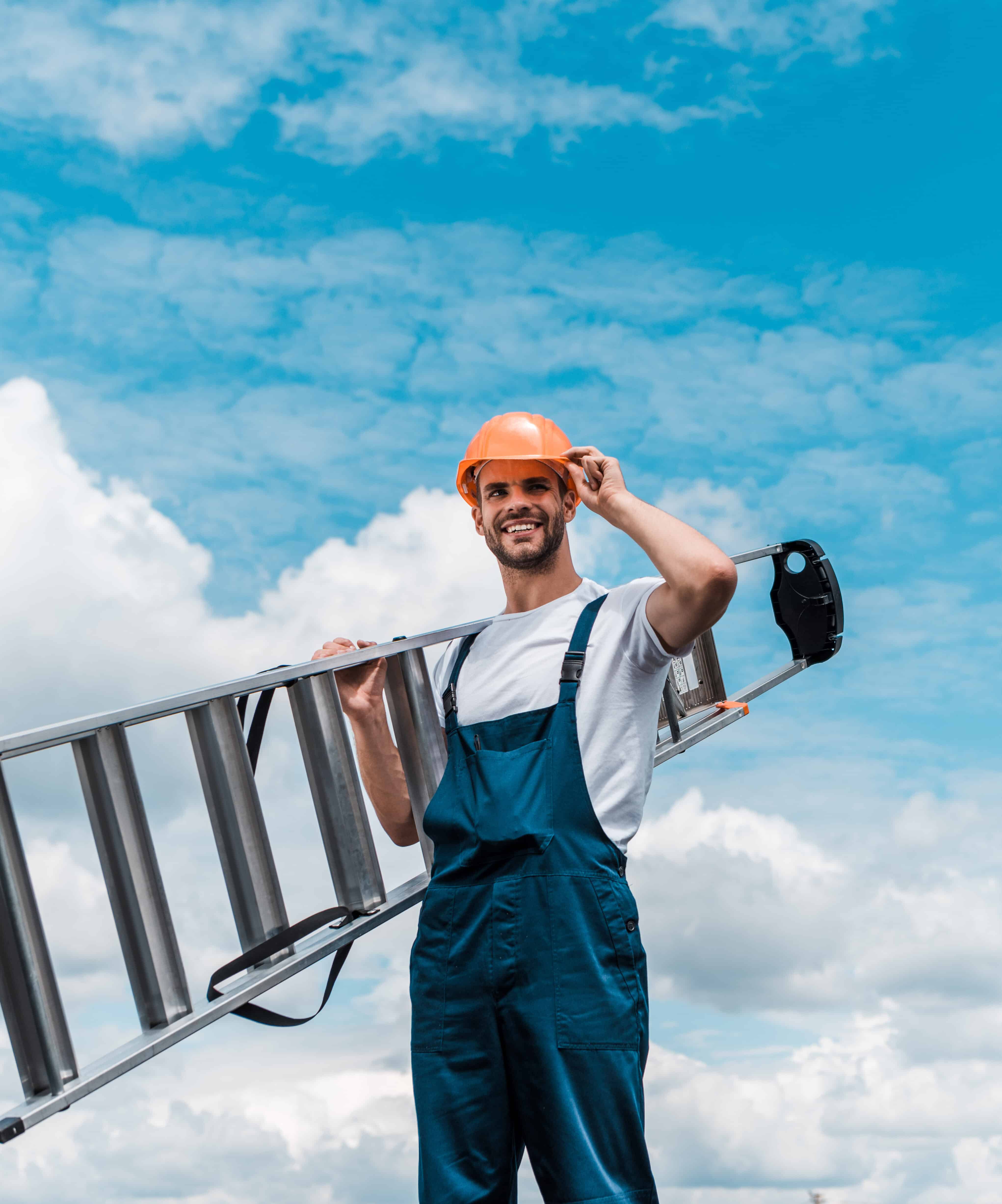 Cheerful repairman holding ladder and smiling against blue sky with clouds