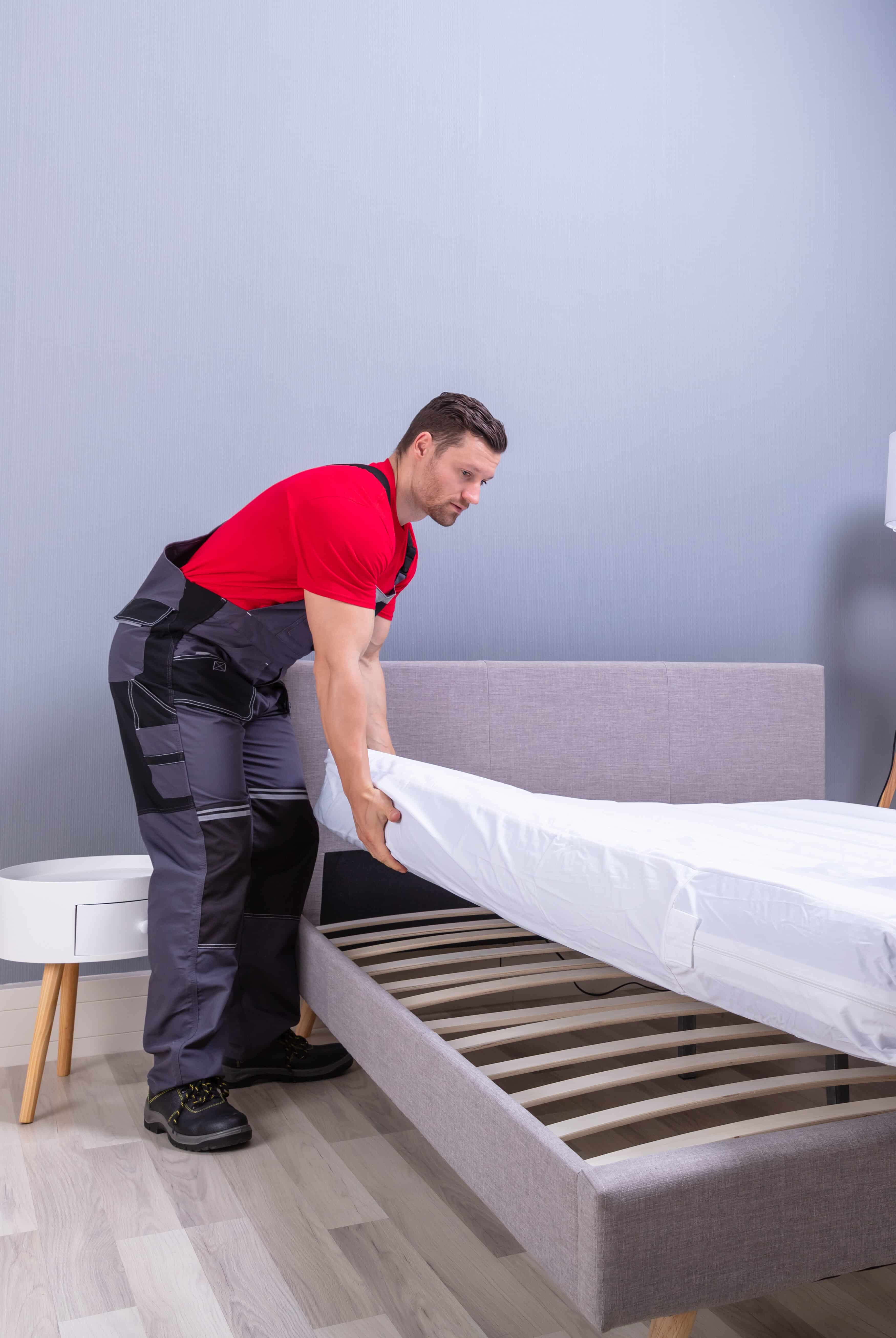 Male Bedroom Installer Professional In Uniform Placing The Mattress Over The Bed In New House