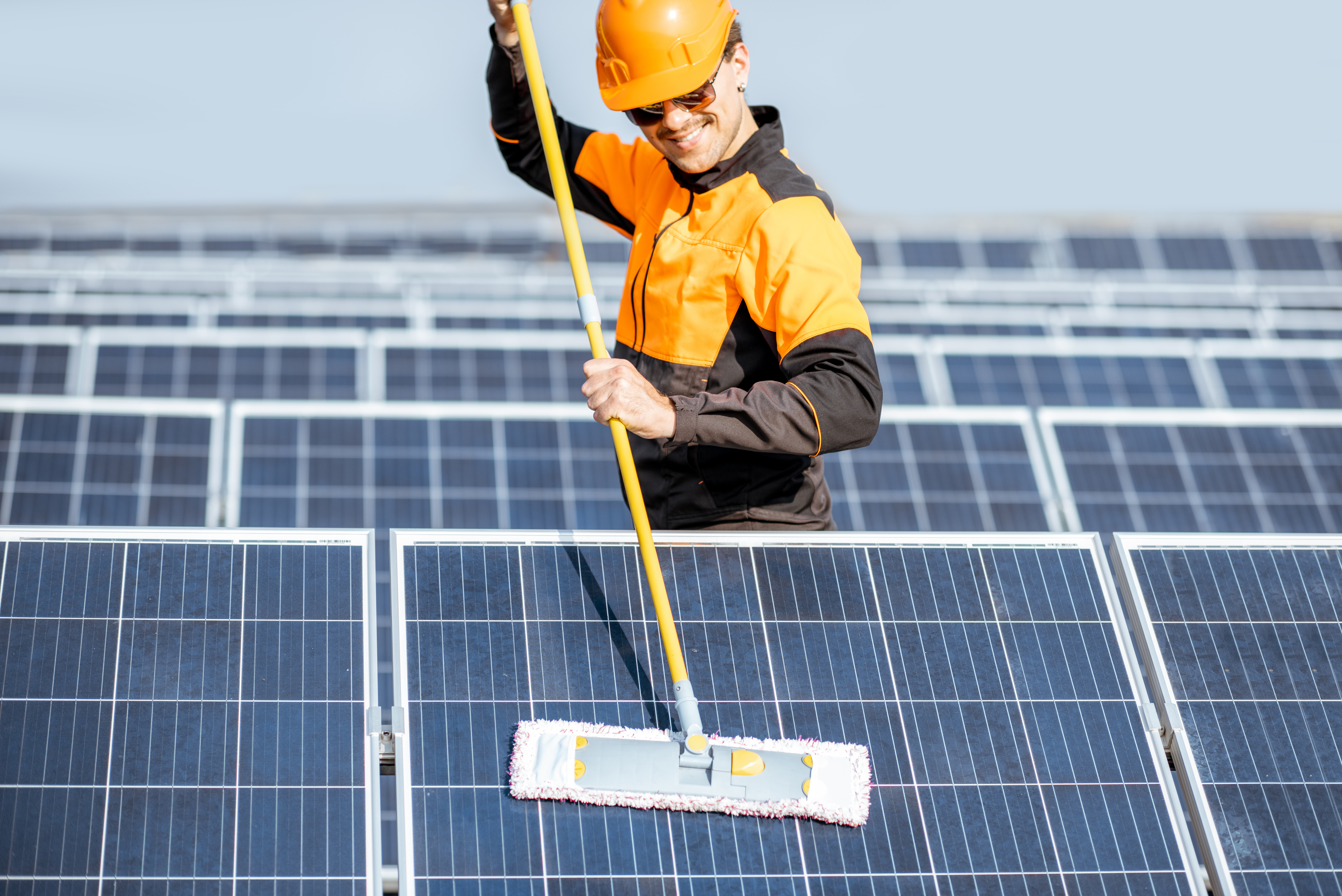 Professional cleaner in protective workwear cleaning solar panels with a mob. Concept of solar cleaning service