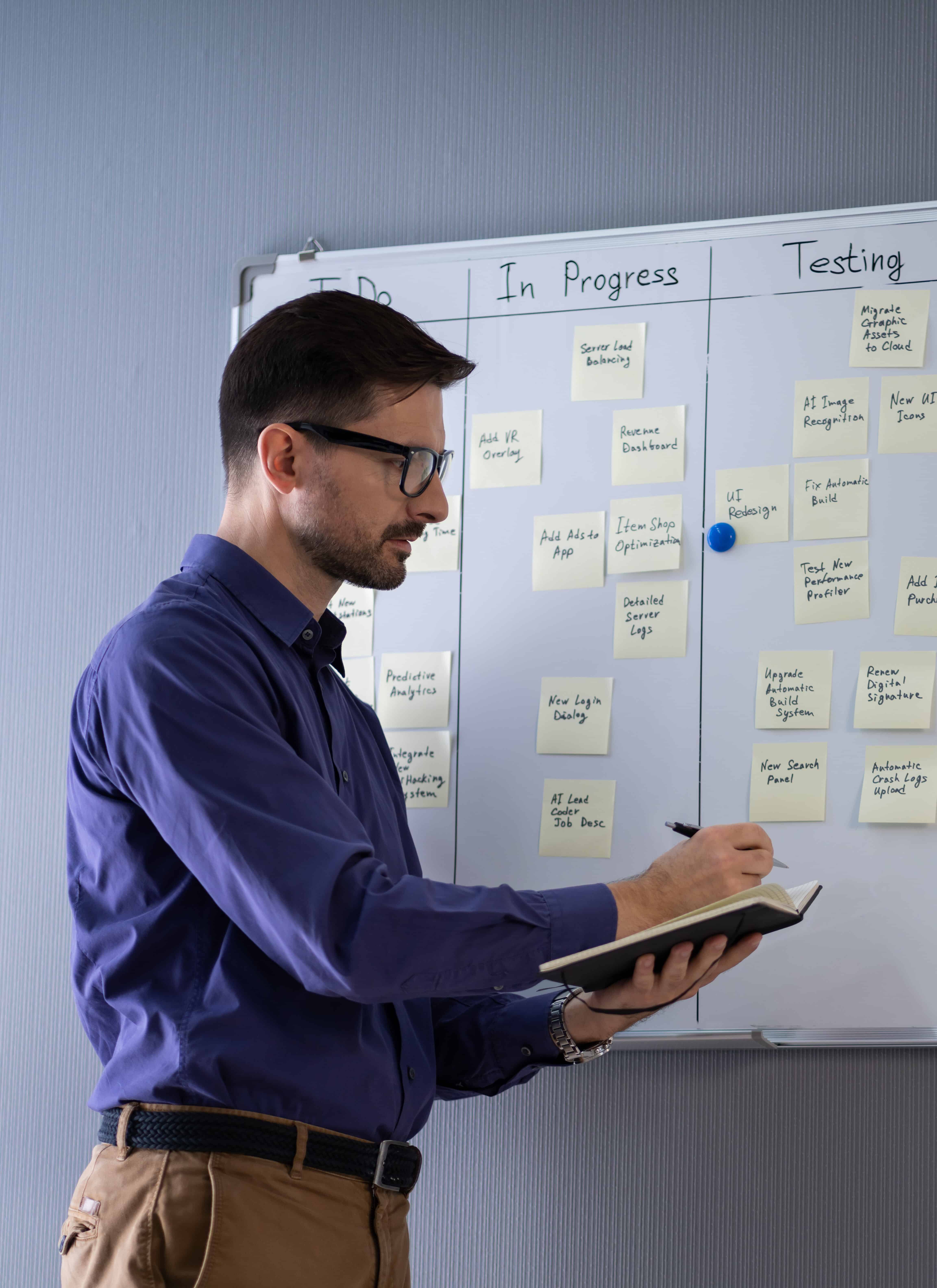 Side View Of a Life Coach Writing On Sticky Notes Attached To White Board In Office