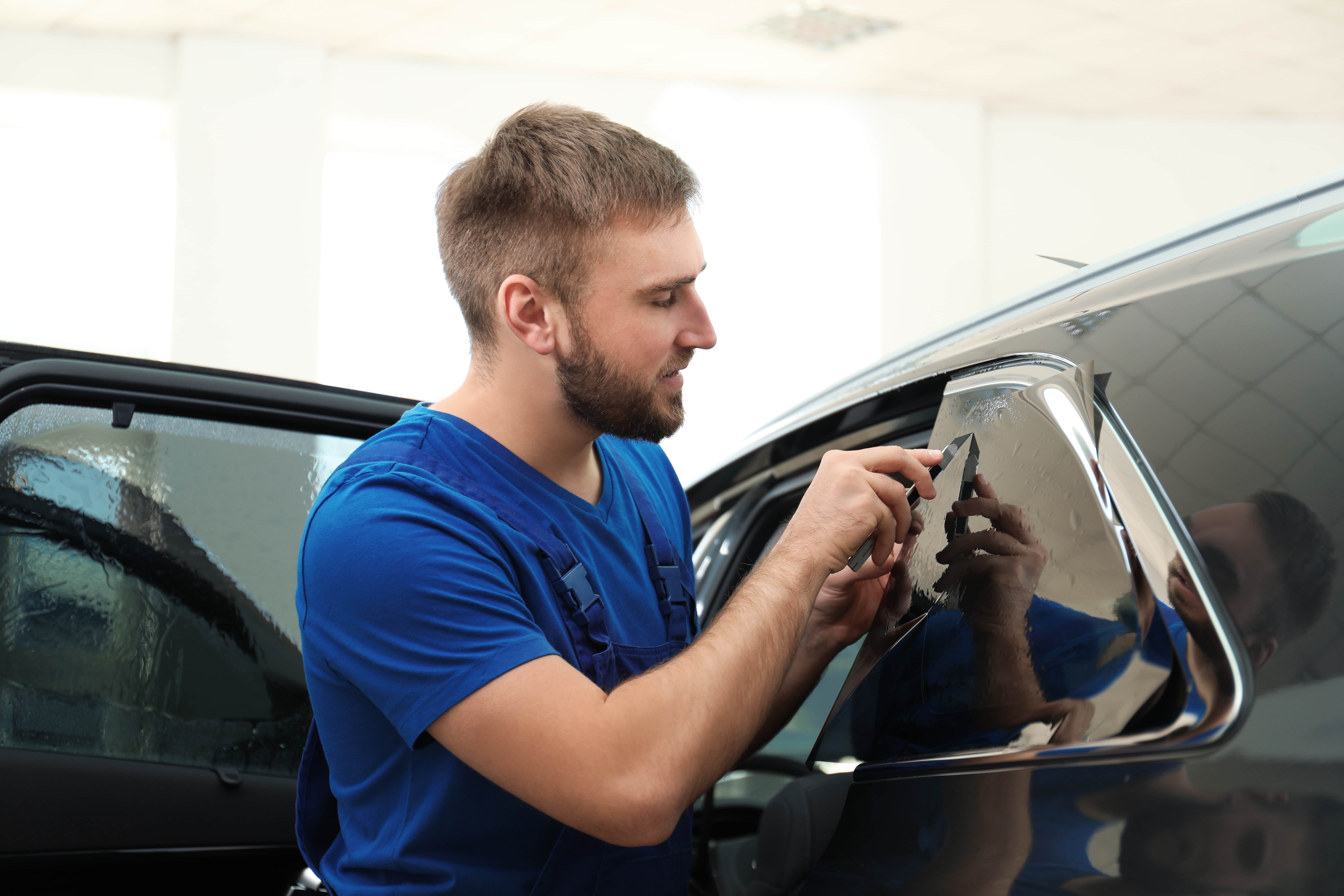 Worker tinting car window with foil in workshop