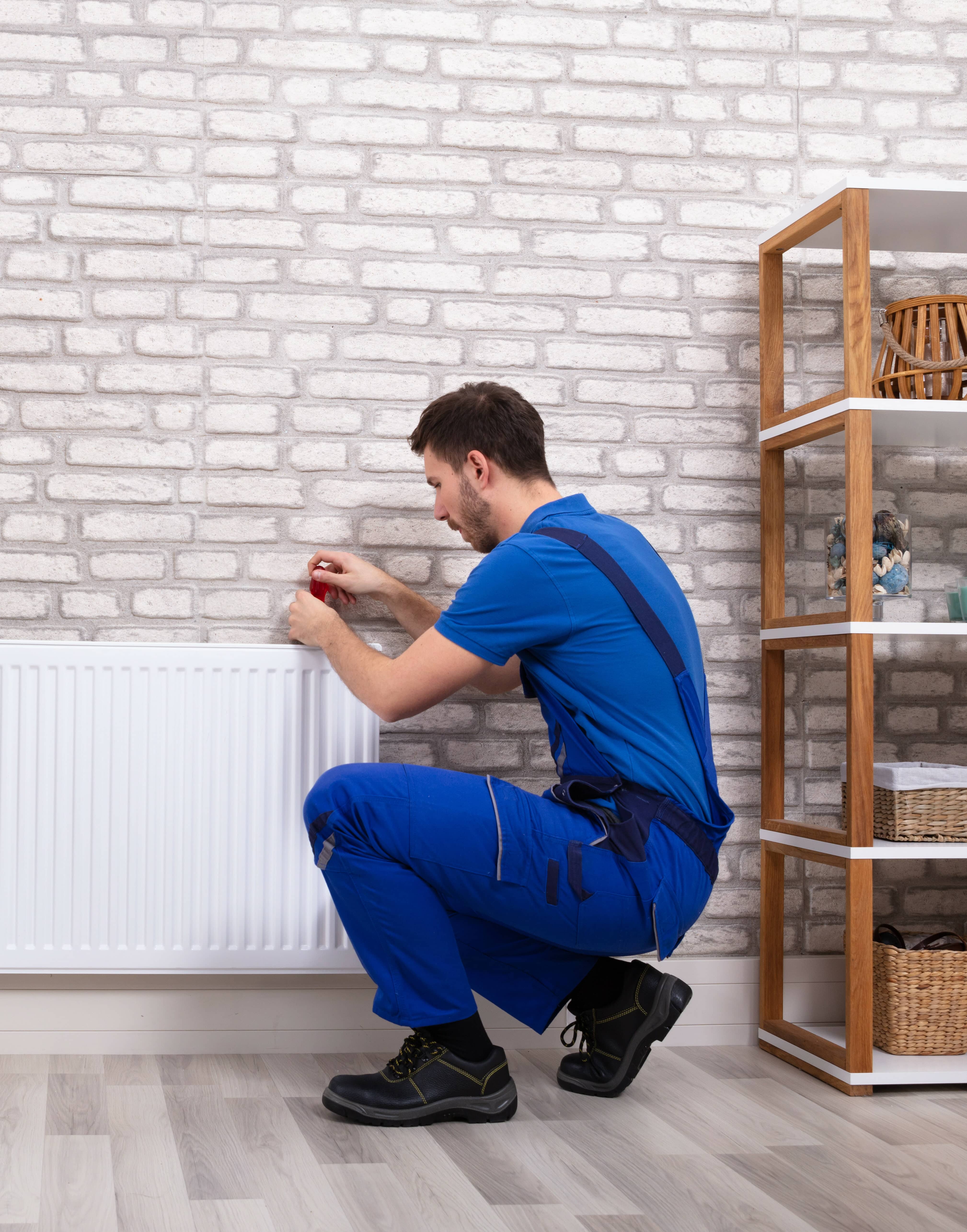 Portrait of a Young Male Plumber In Uniform Installing a Electric Heating With Screwdriver