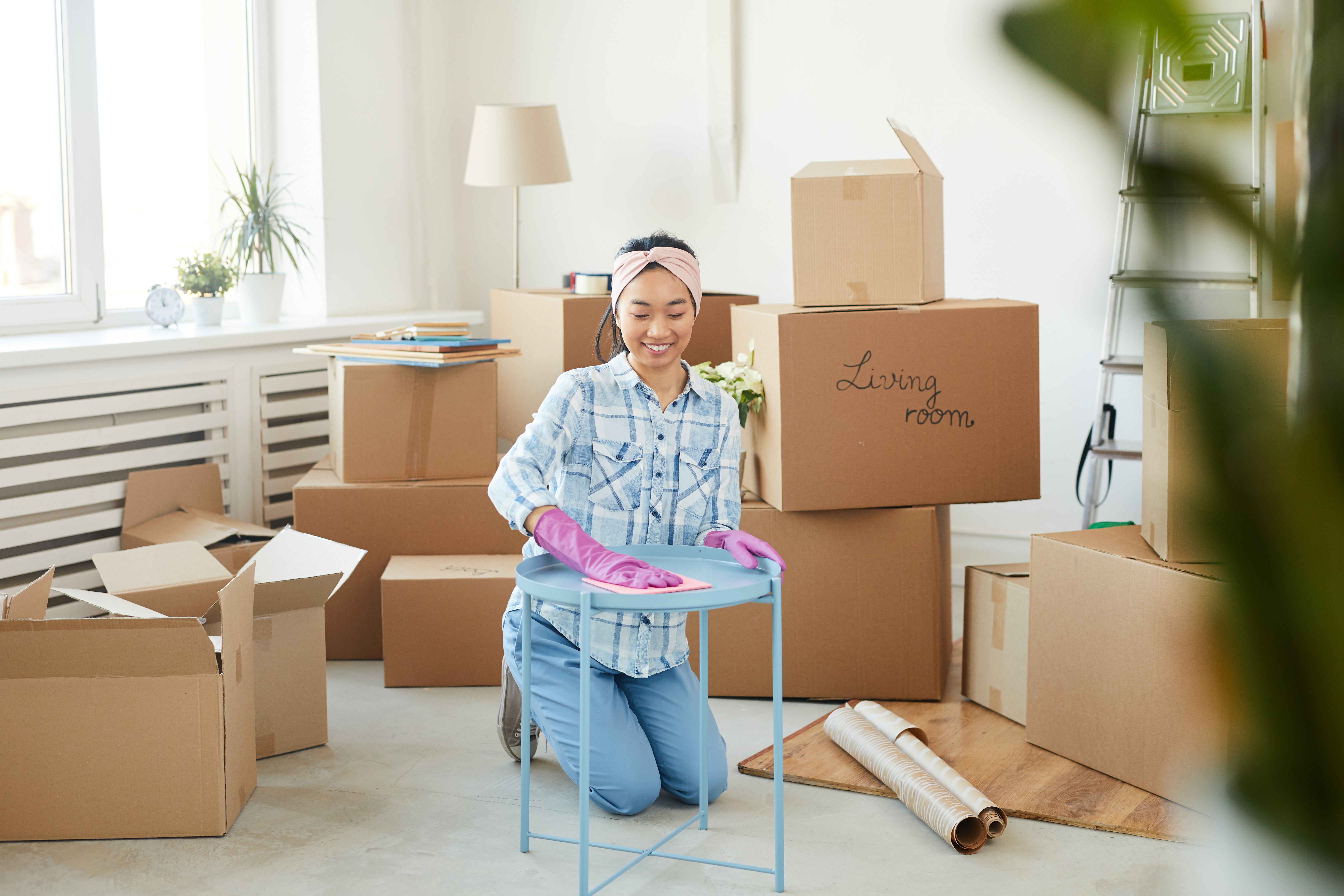 Full length portrait of cheerful Asian woman working in a Decluttering Service, cleaning furniture while moving into new house with boxes in background