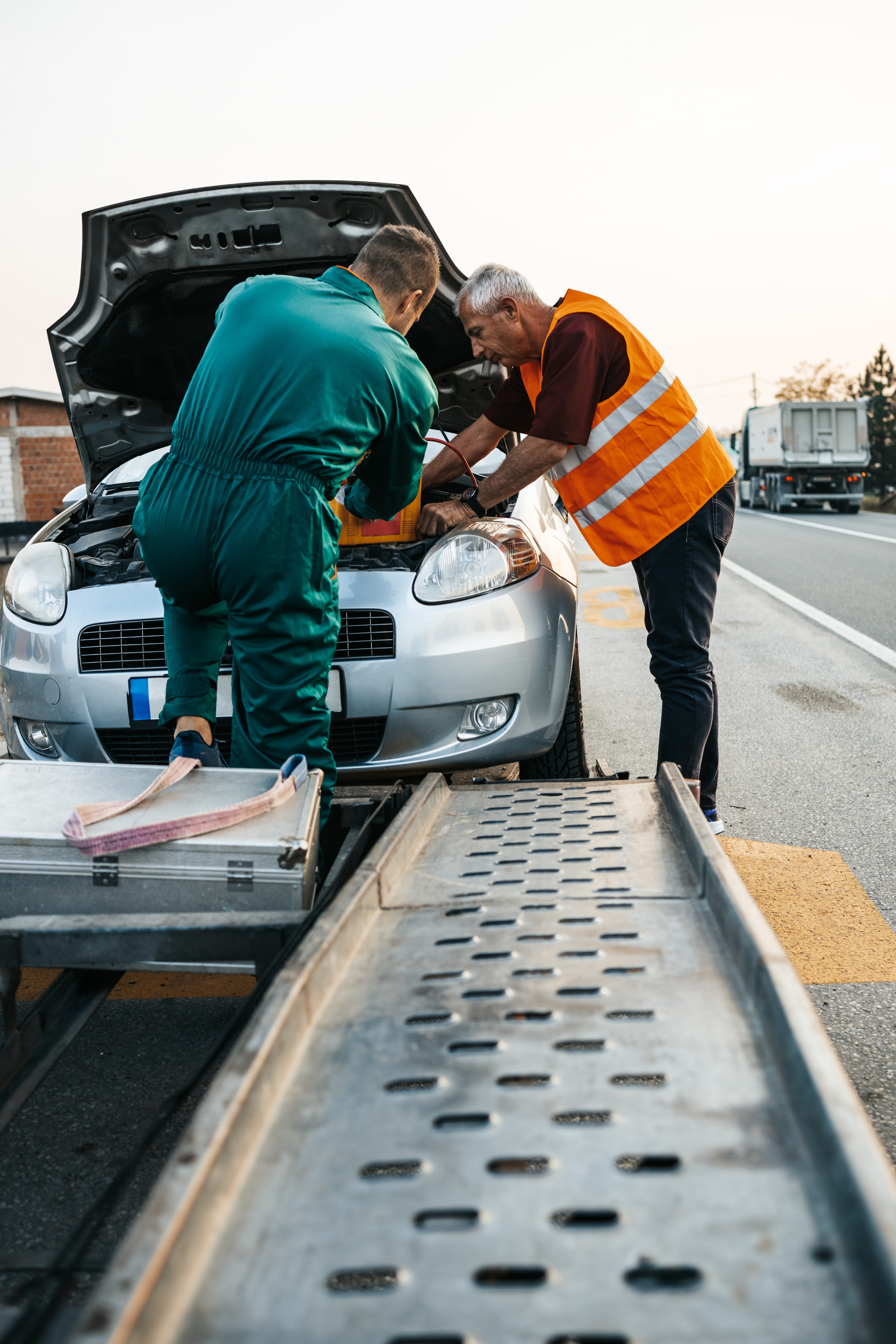 Two road assistant workers in towing service trying to start car engine with jump starter and energy station with air compressor. Roadside Car Towing