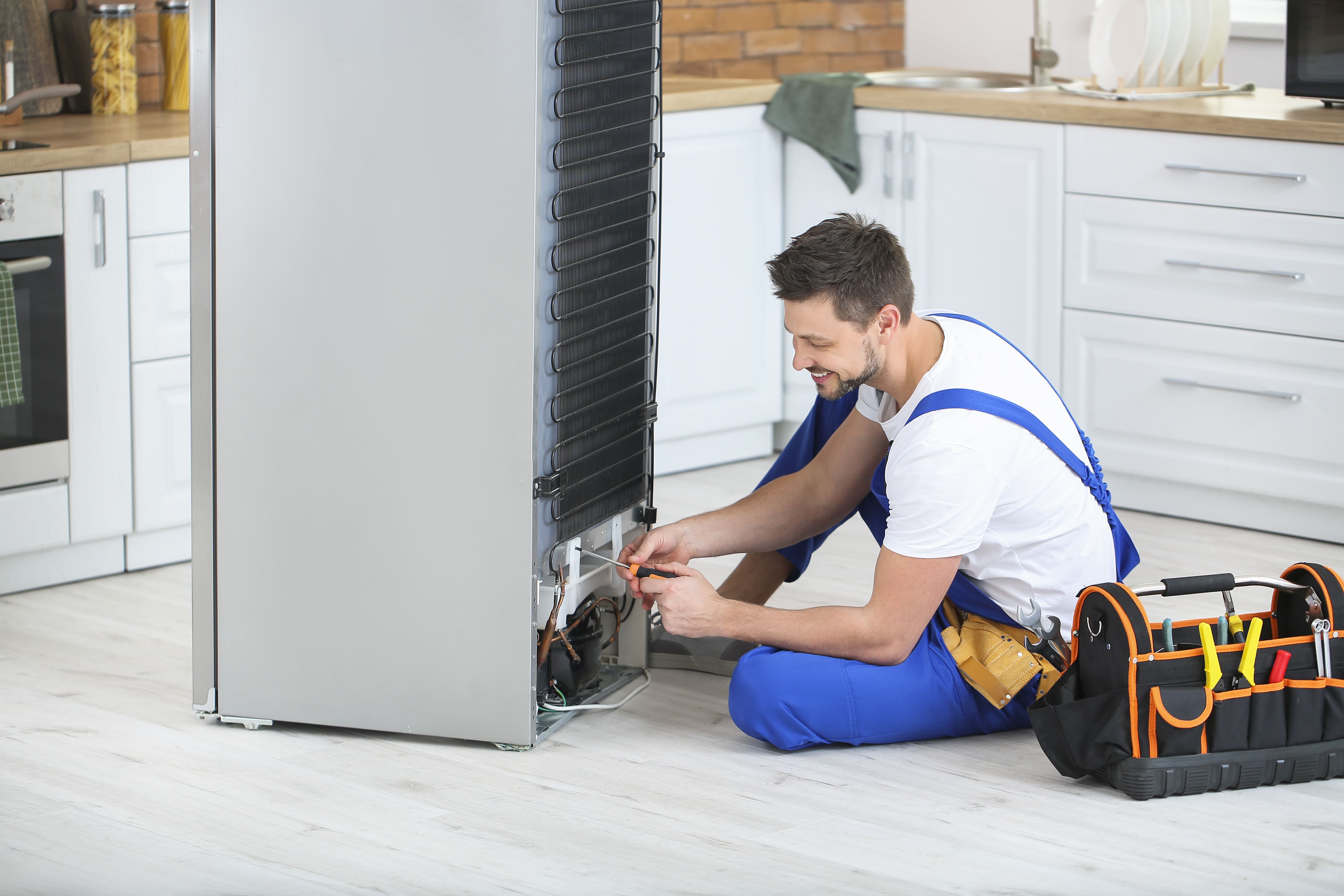 Worker repairing refrigerator in kitchen