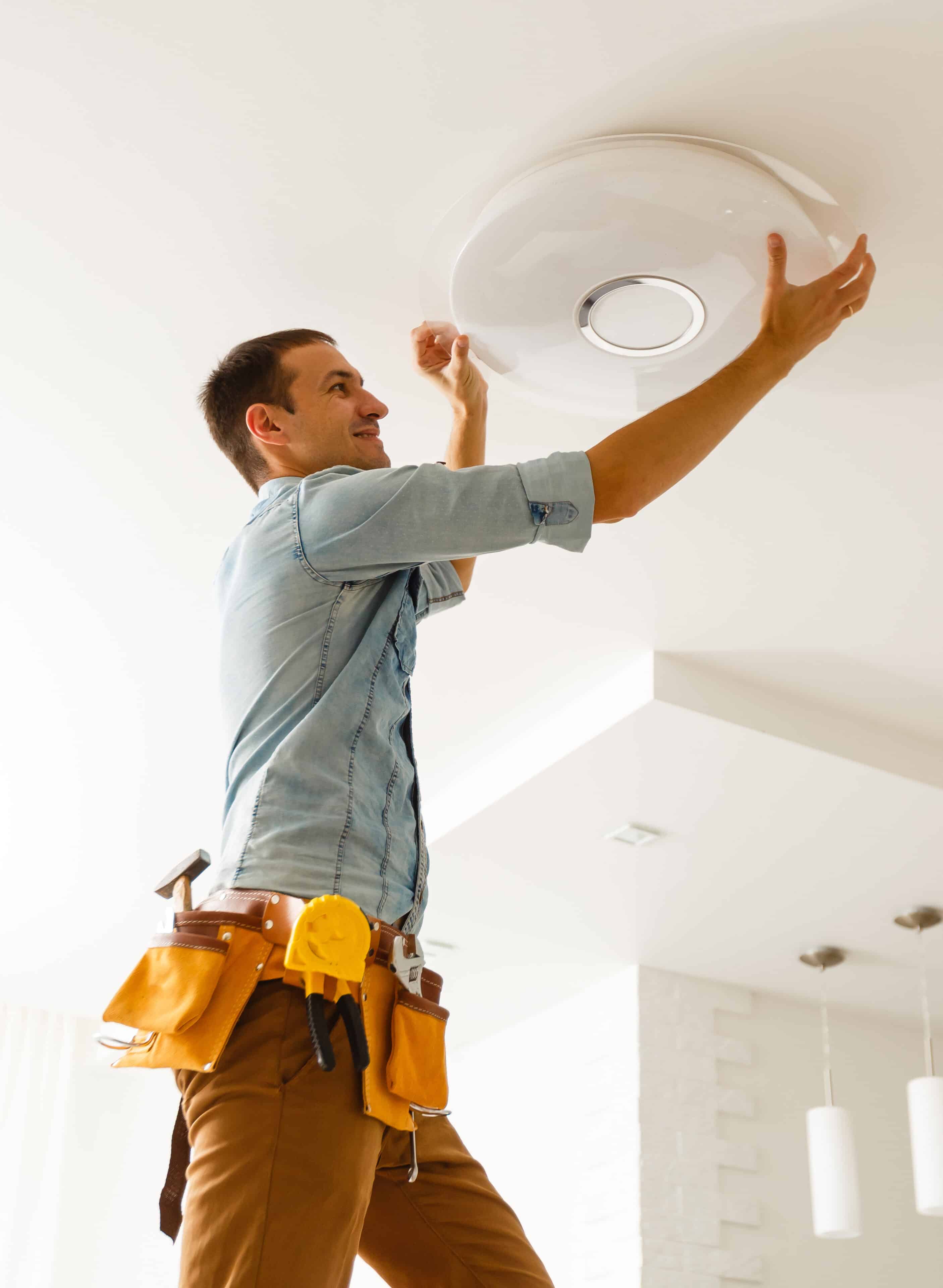 Electrician is installing and connecting a lamp to a ceiling, doing a LED Lighting Upgrade