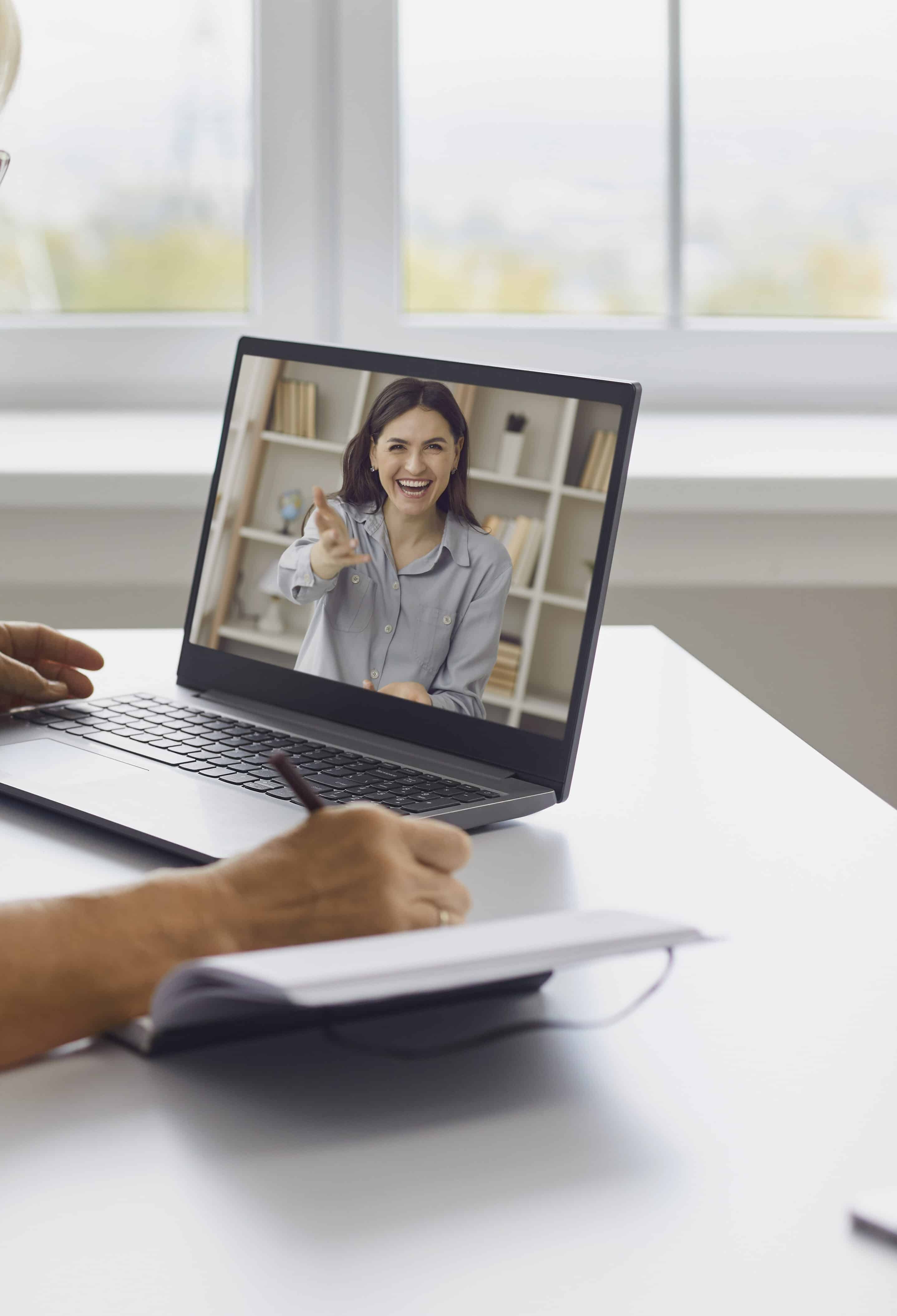 Happy mature lady having video call with personal motivational coach. Senior woman sitting at desk at home, watching webinar on laptop, listening to online lecture, learning new stuff and taking notes