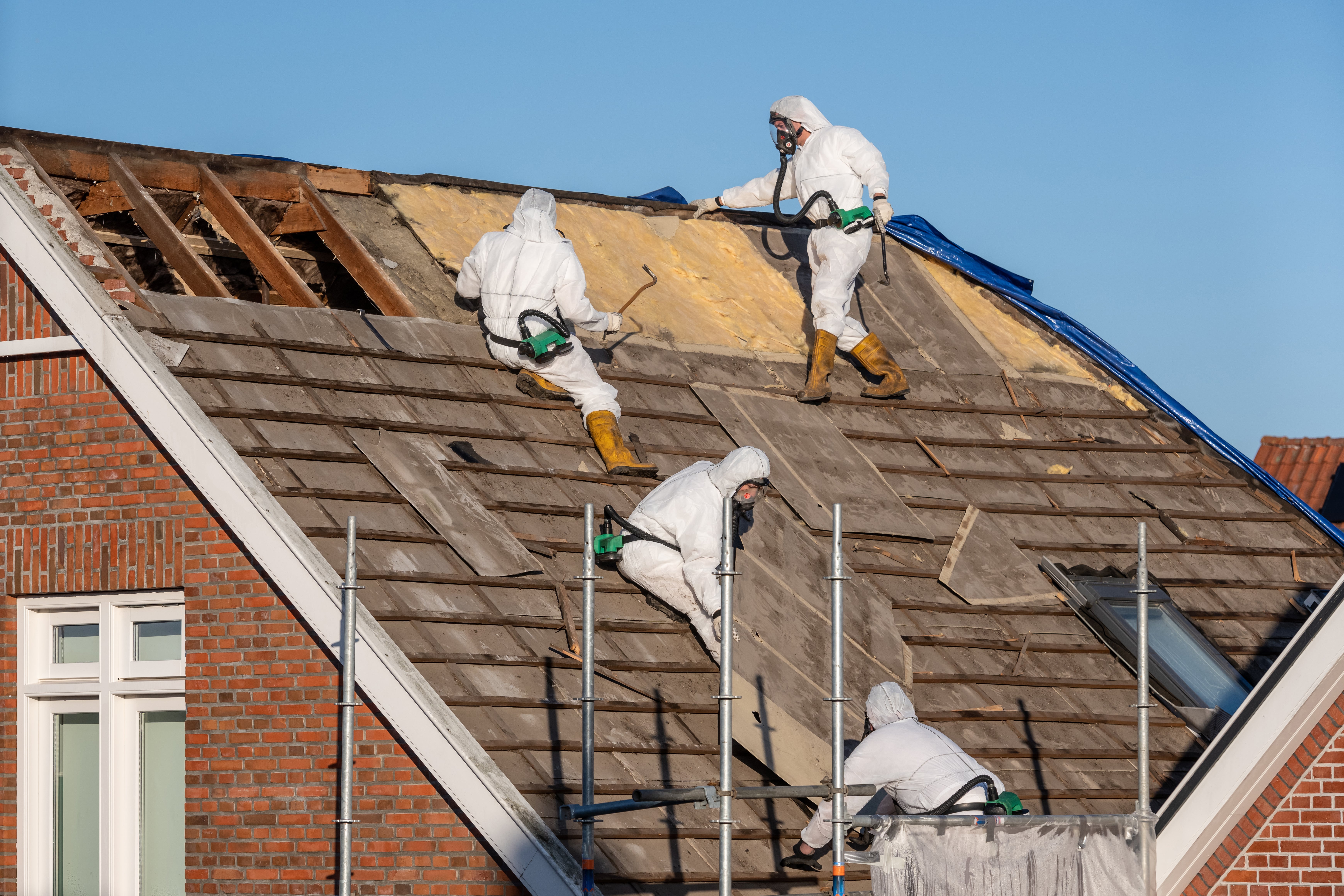 Professionals in protective suits remove asbestos-cement roofing underlayment