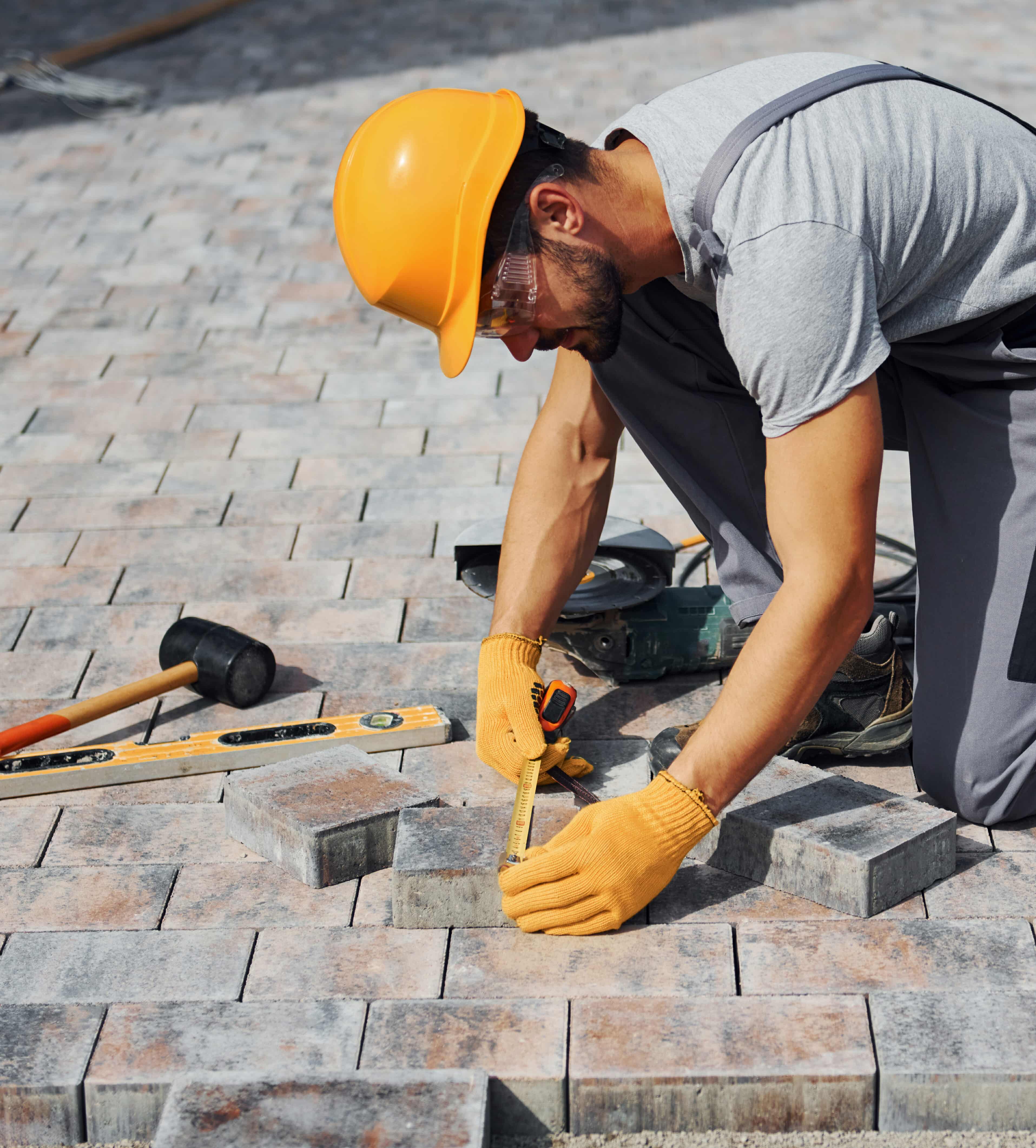 Measuring process. Male worker in yellow colored uniform have job with pavement.