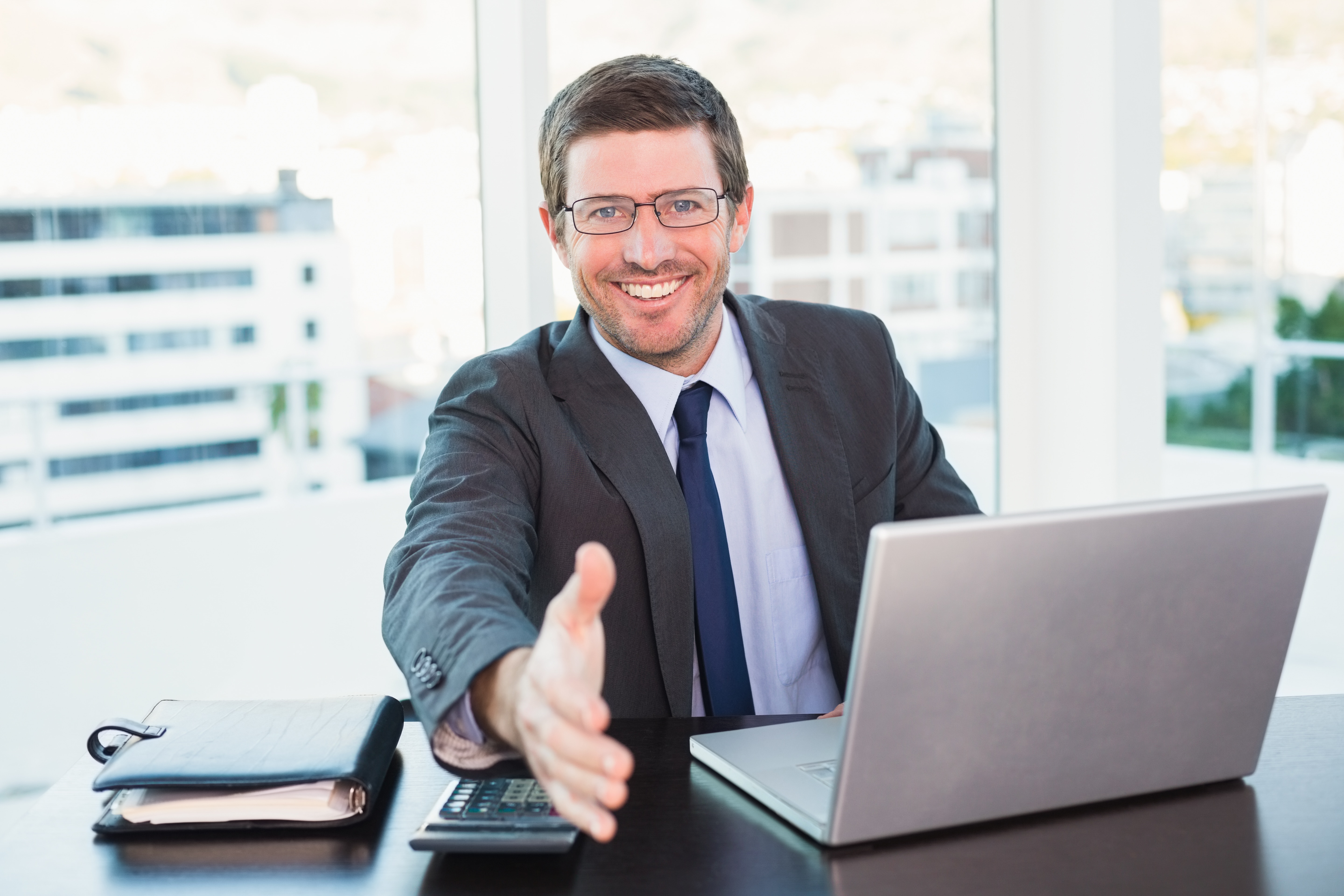 Happy businessman offering his hand in his office