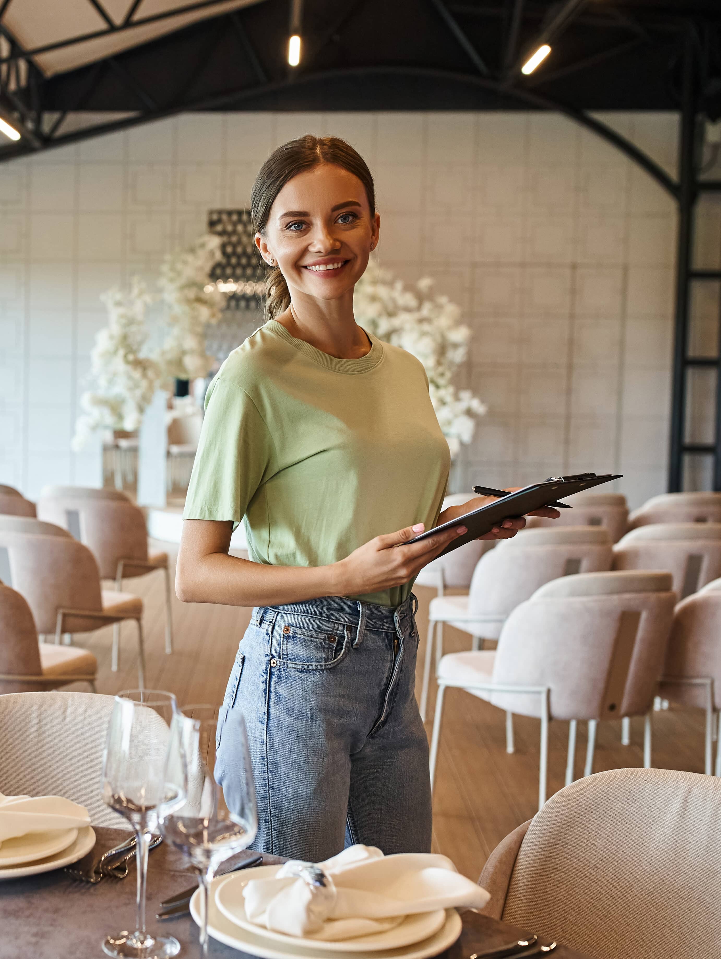 Happy corporate event manager planner with clipboard smiling at camera near festive table