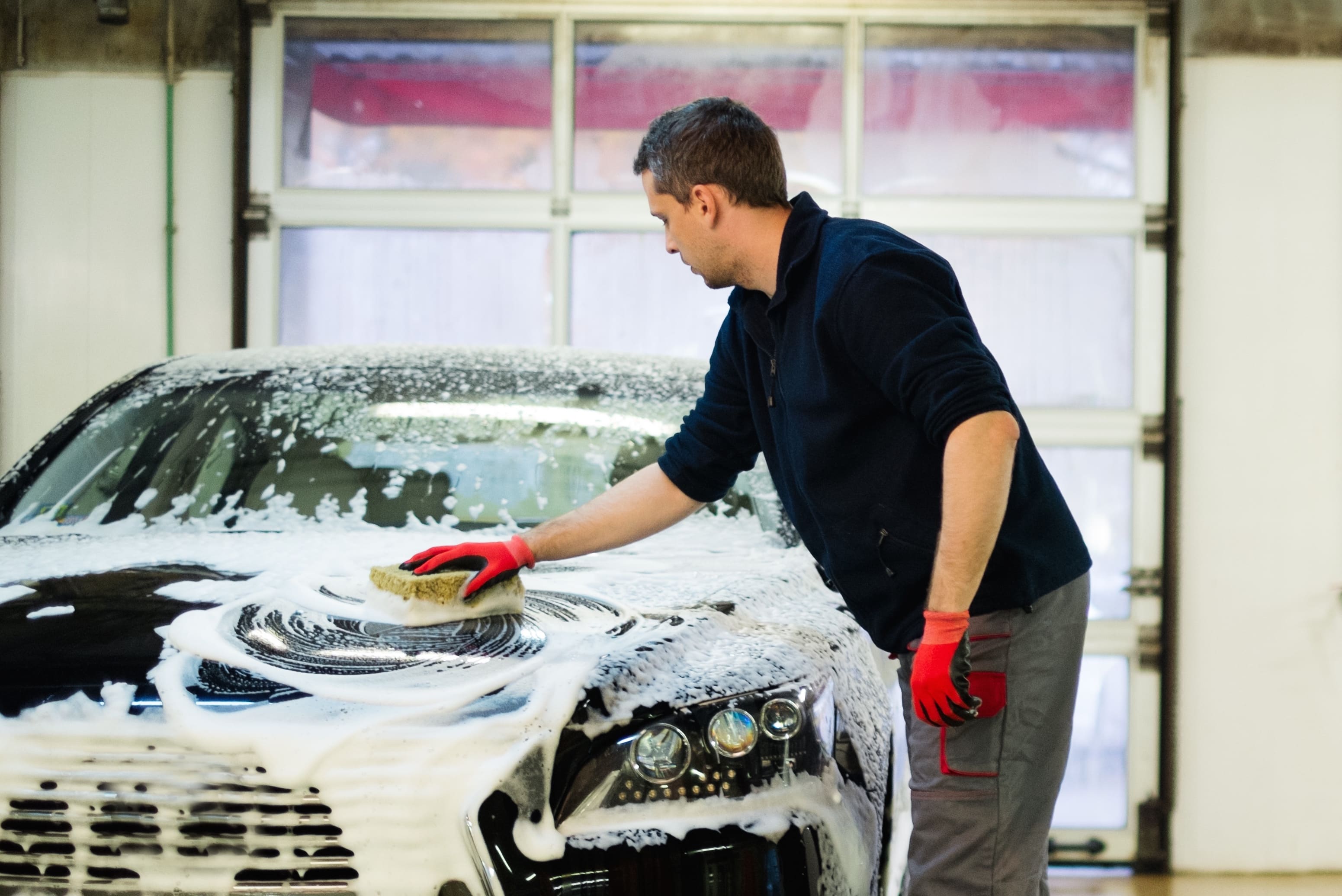 Man worker washing luxury car with sponge on a car wash