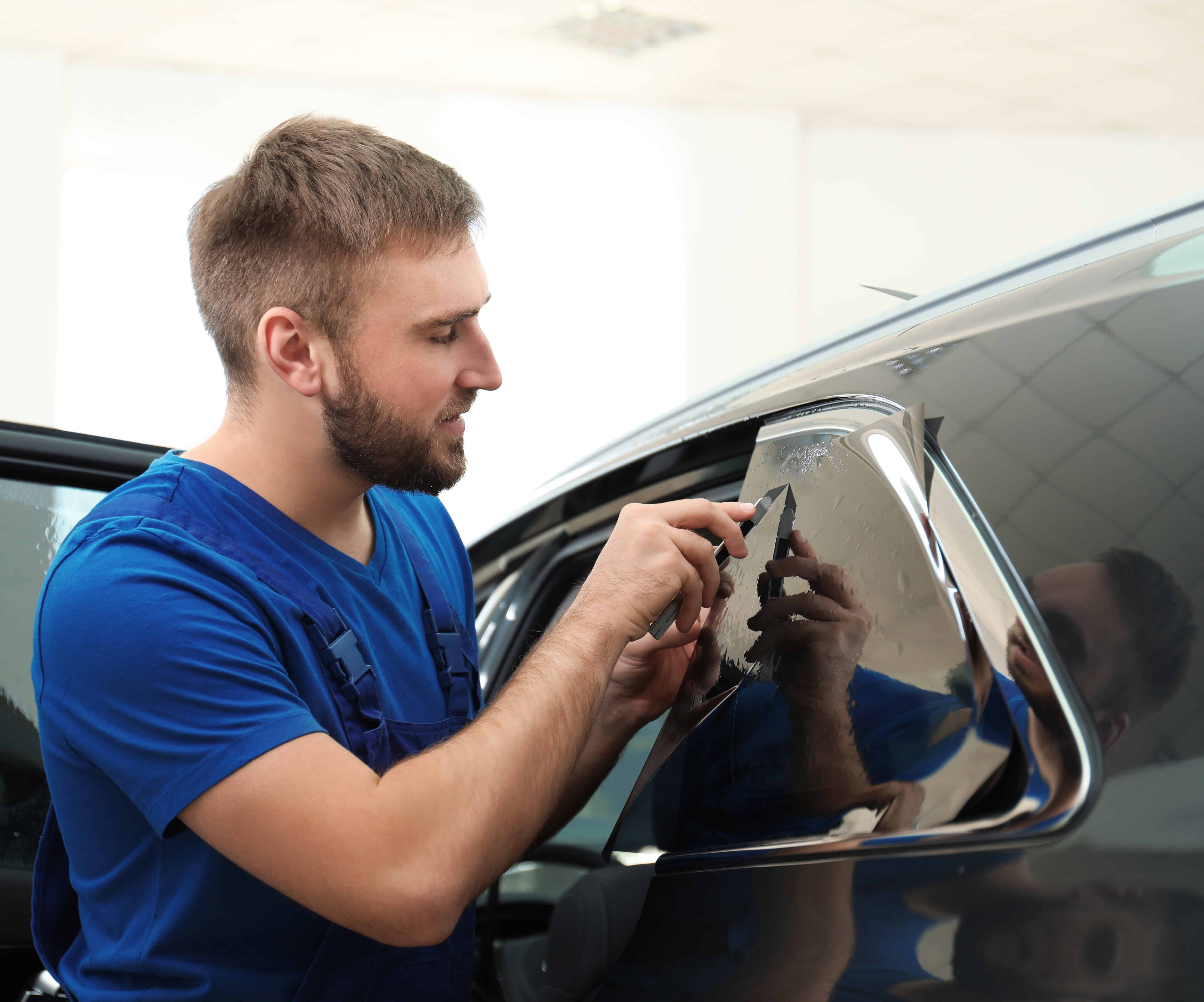 Worker tinting car window with foil in workshop