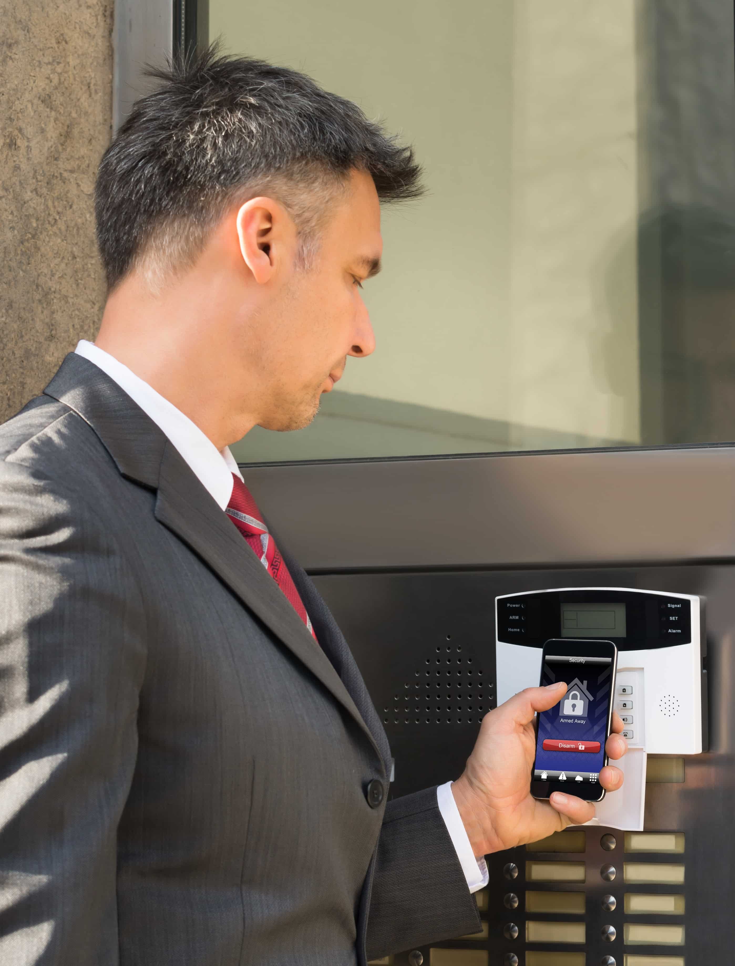 Portrait of a Mature Businessman Holding Smartphone installling a Security System Of Door