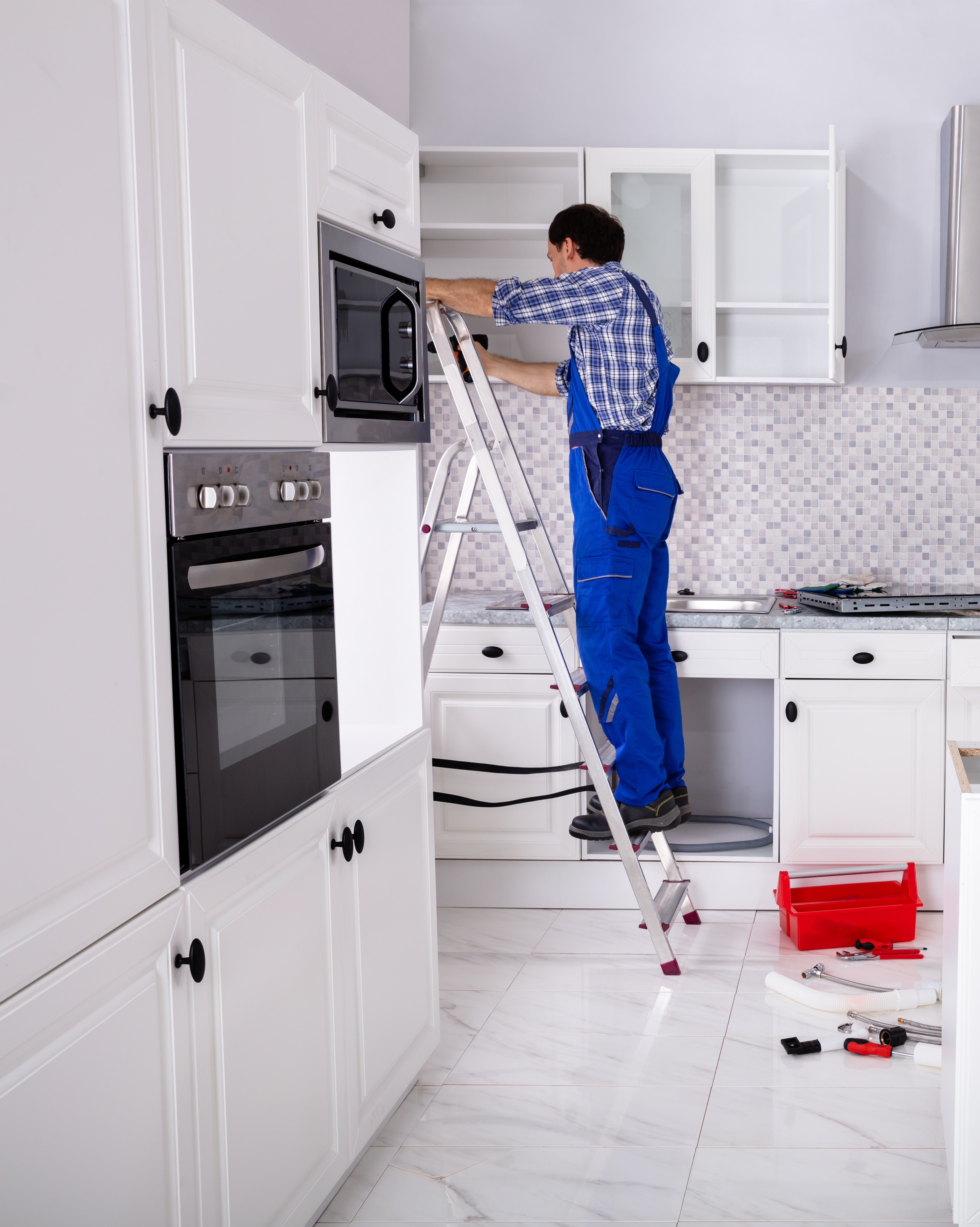 Portrait of Kitchen Specialist Man On Ladder Adjusting Cabinet Door Hinge On Kitchen Cabinet