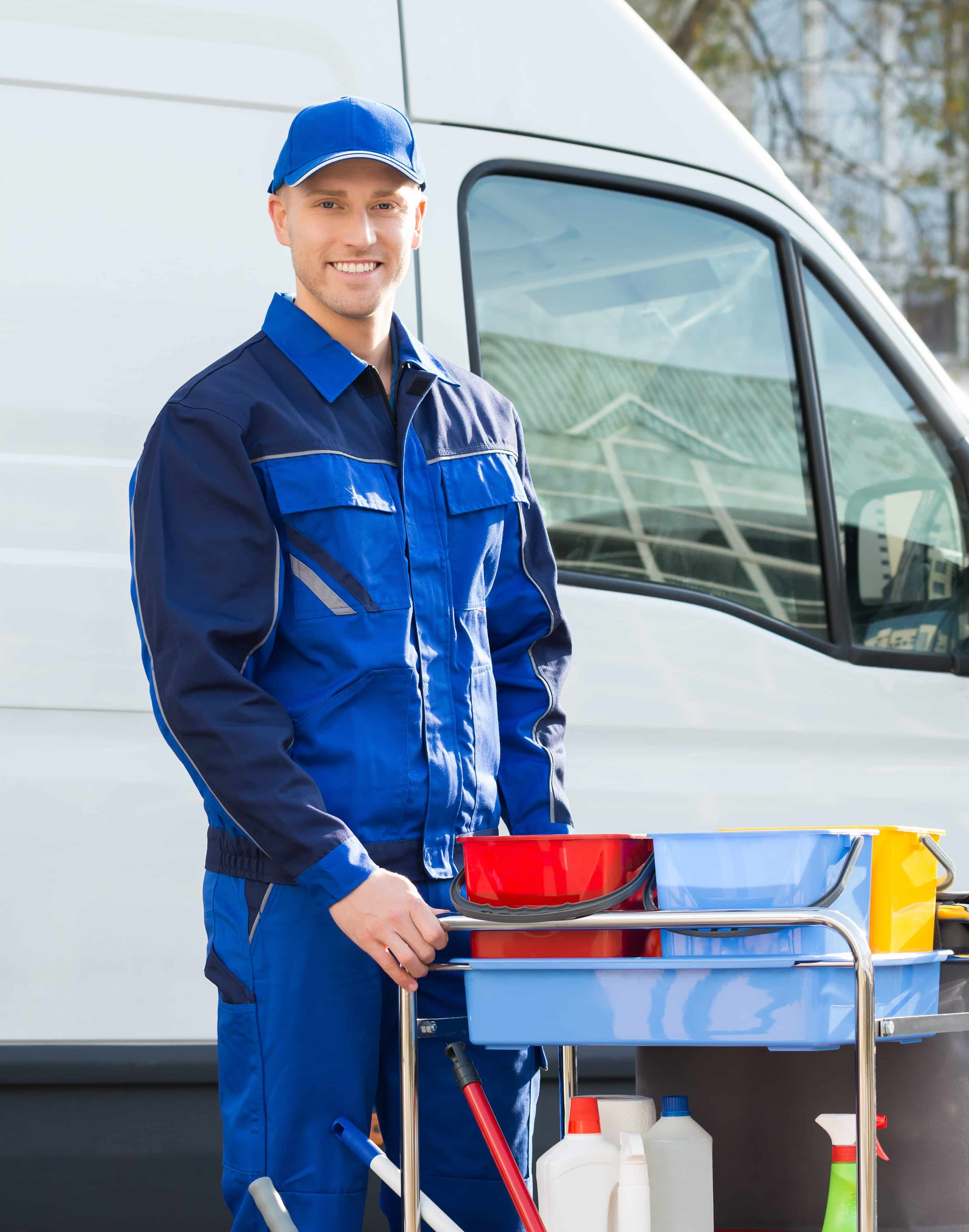 Portrait of happy end of lease cleaner male janitor standing with cleaning equipment against truck