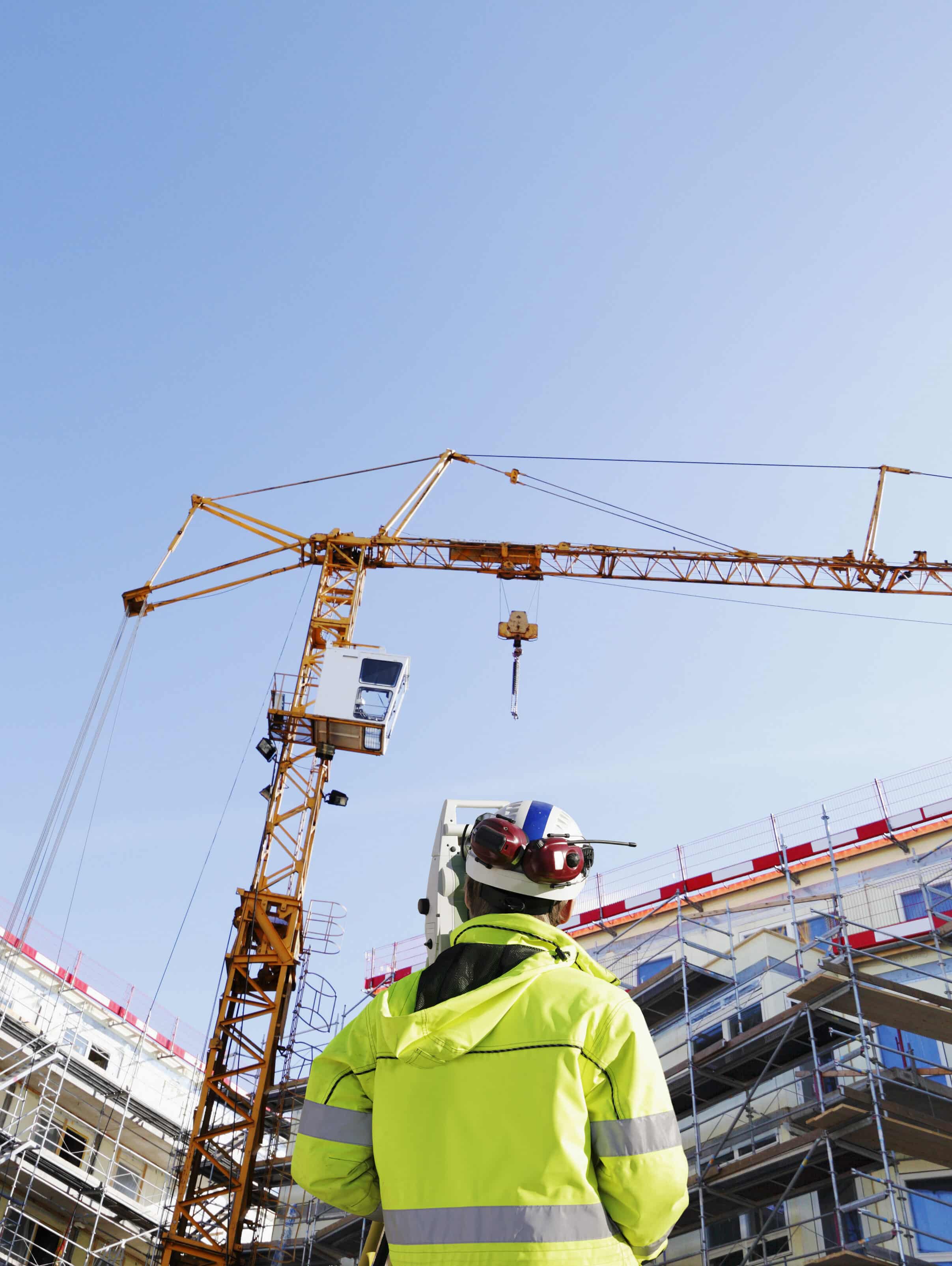 Portrait of a Surveyor with measuring instrument inside building site with a Crane in th back