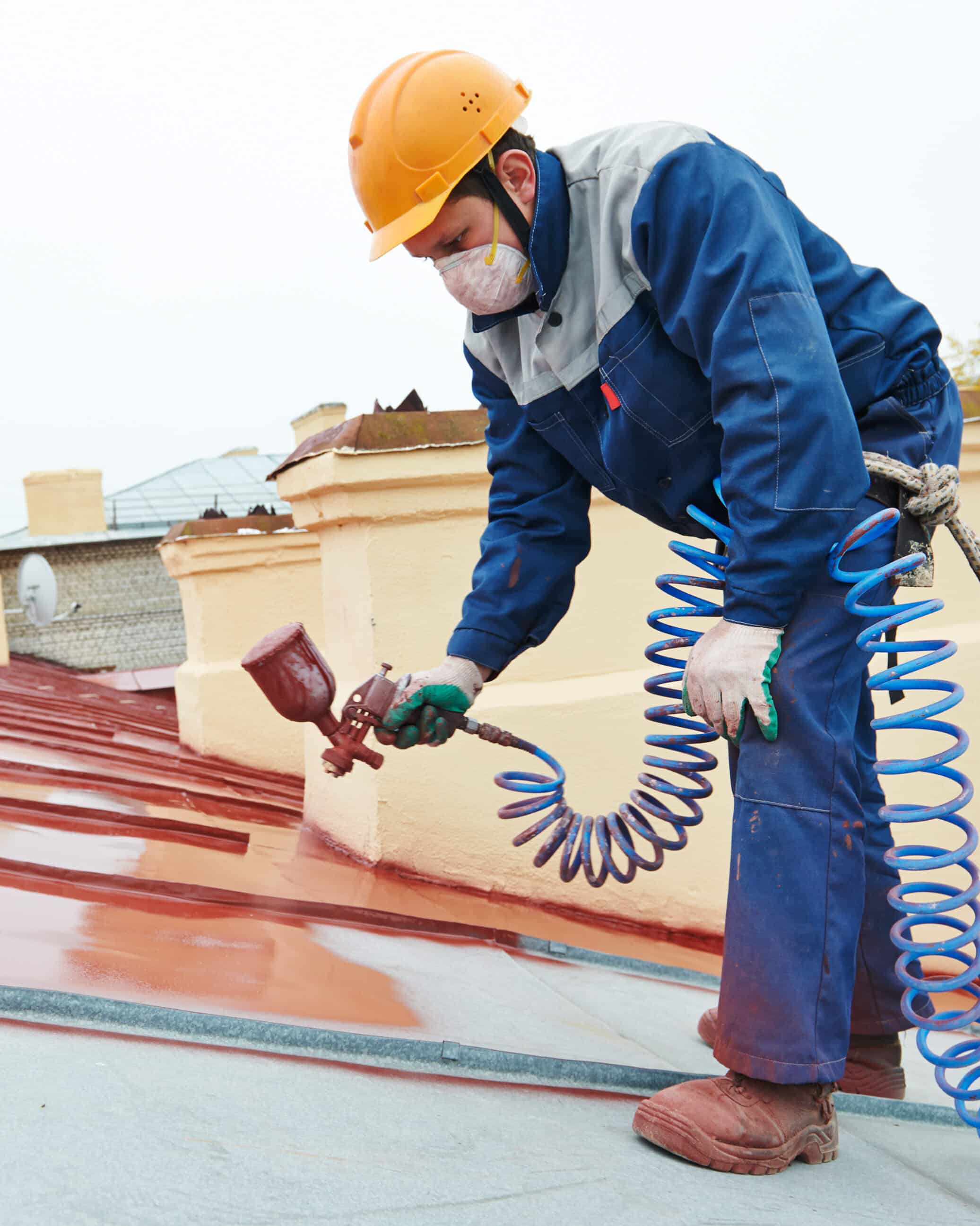 roofer builder worker with pulverizer spraying paint on metal sheet roof