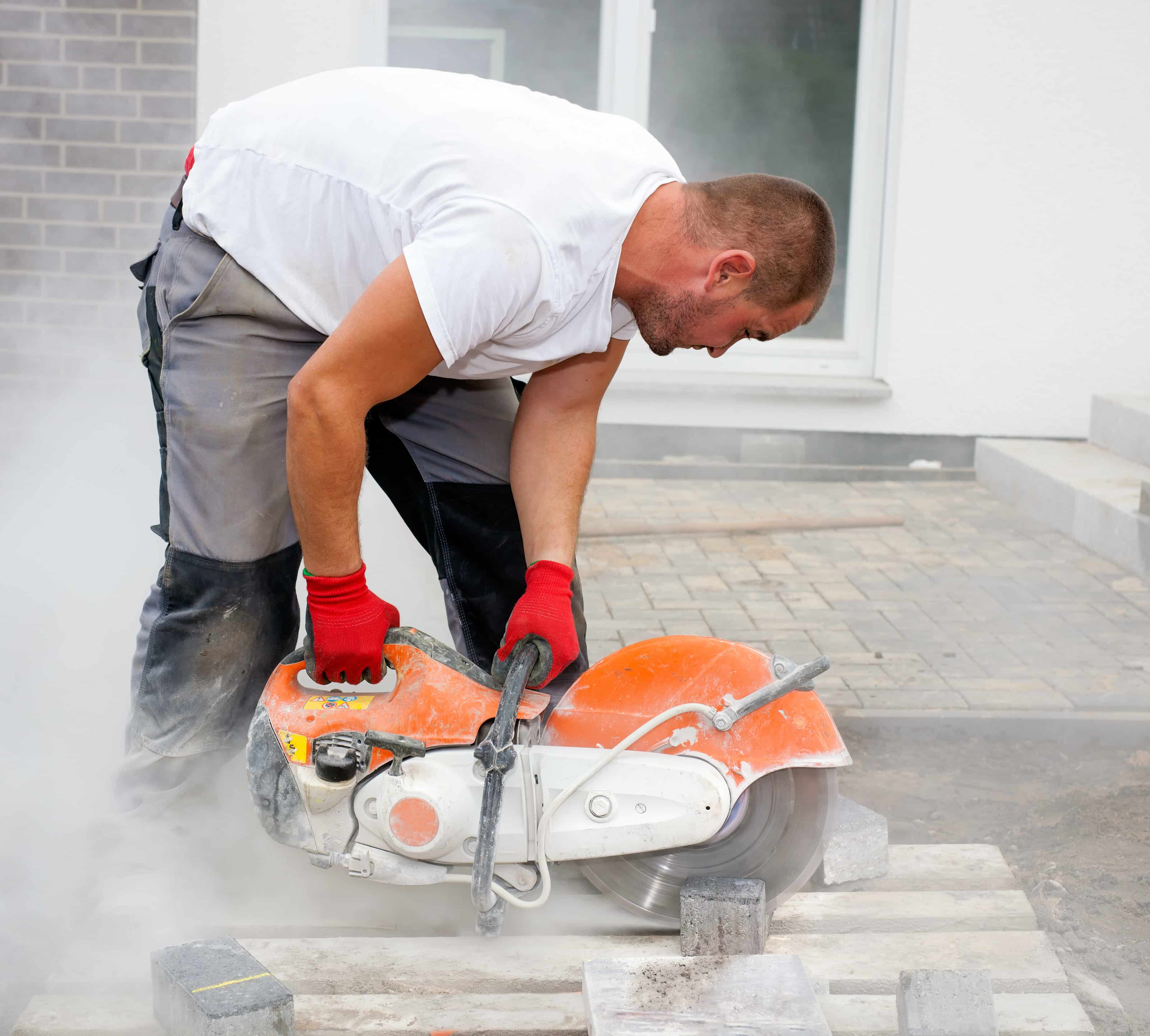 Construction worker using a concrete saw, cutting cutting in a cloud of concrete dust for creating a track.