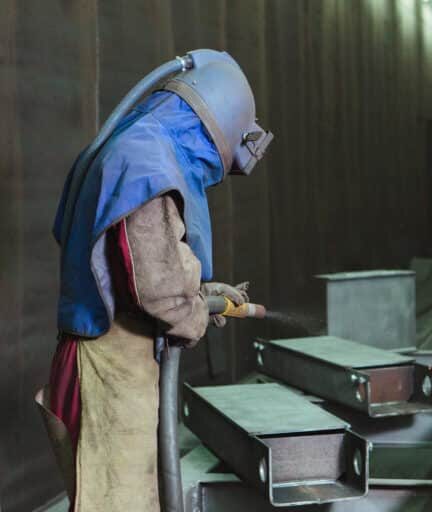 Sandblast. Blasting metal. An employee prepares a metal part for painting. A harsh man works in the factory.