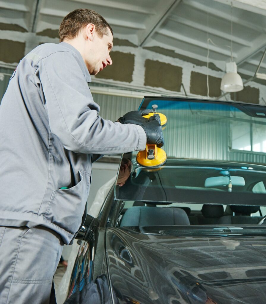 Windscreen Replacement mechanic worker replaces windshield or windscreen on a car in automobile workshop garage