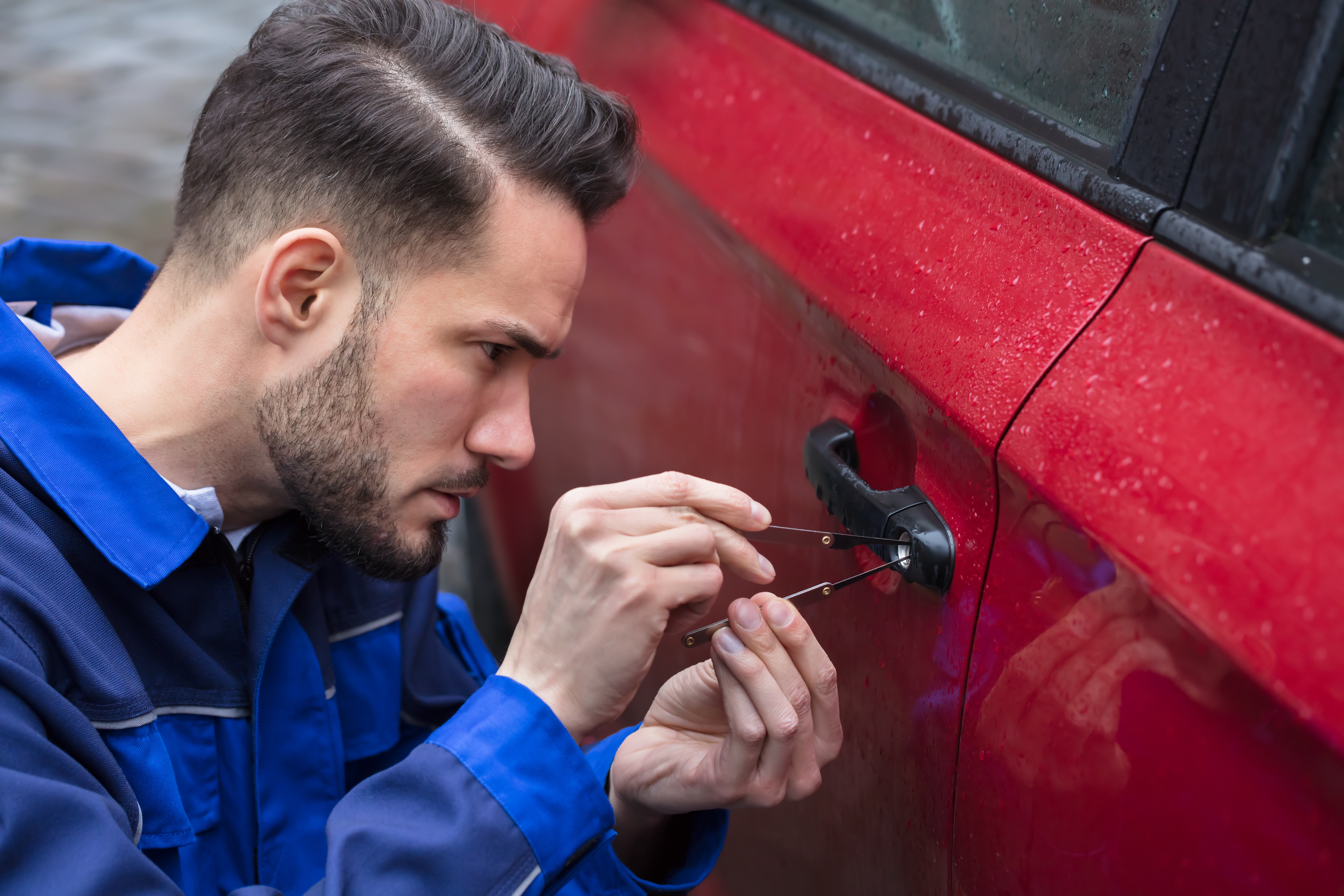 Portrait of a Young Man Car Locksmith Opening Red Car Door With Lockpicker