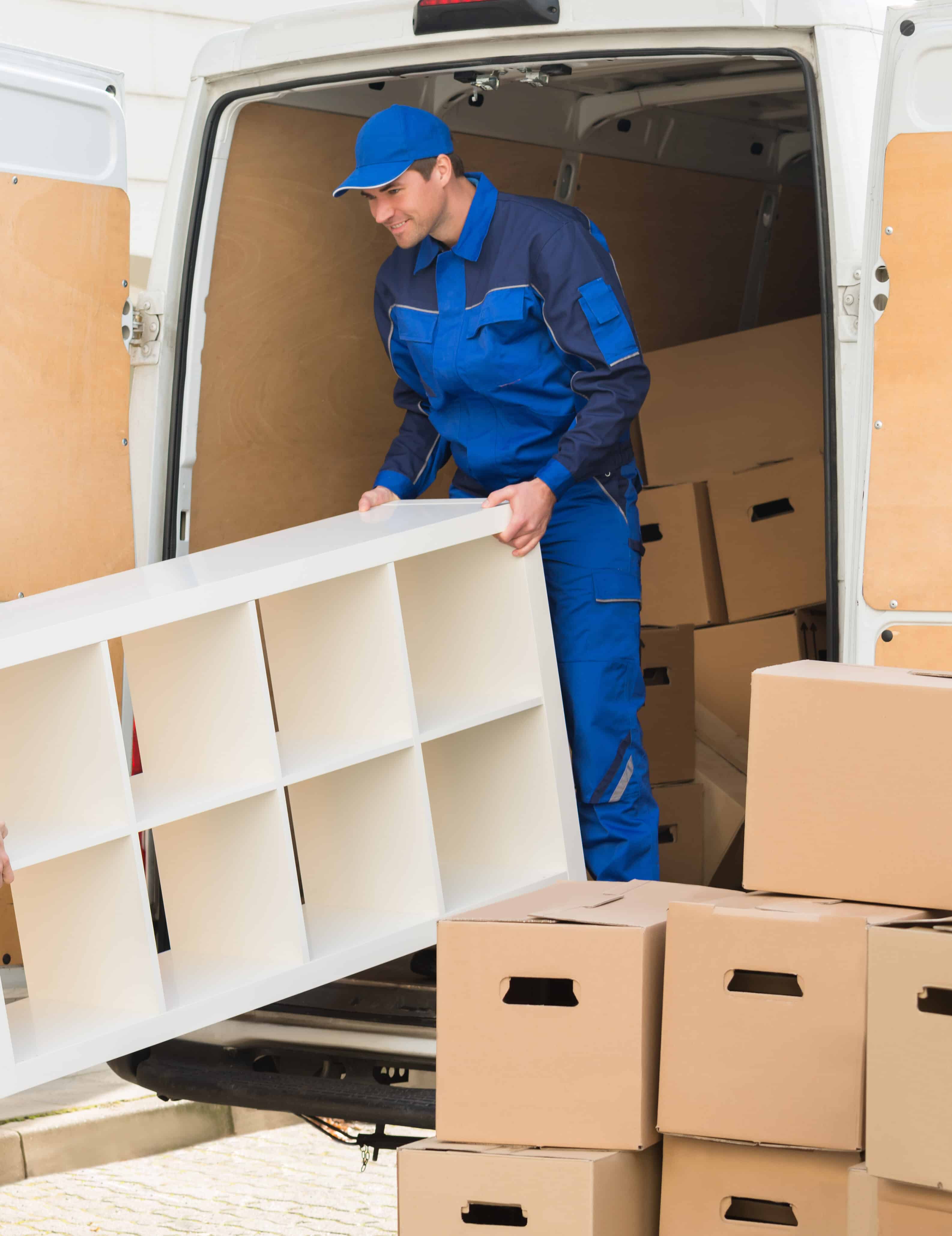 Young male movers unloading furniture and cardboard boxes from truck on street